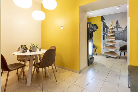 A seating area with a white round table, four brown chairs, three pendant lights, a vending machine, and decorative wooden spiral at B&B Hotel Roma San Lorenzo Termini