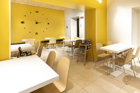 Dining area with white tables, wooden chairs, bright yellow accent walls with a large wall clock at B&B Hotel Roma San Lorenzo Termini