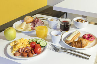 Breakfast spread on white tables with scrambled eggs, sausage, fruit, pastries, coffee, and juice at B&B Hotel Roma San Lorenzo Termini