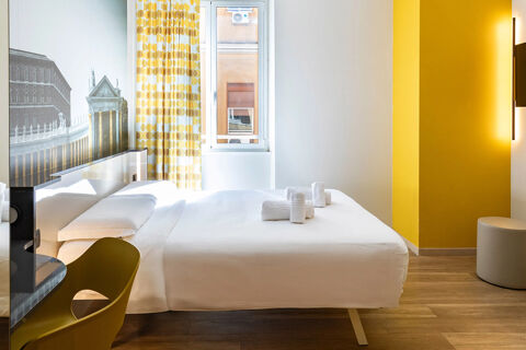 Bedroom with white bed linens, folded towels, yellow chair, patterned curtains, and wall art at B&B Hotel Roma San Lorenzo Termini