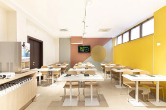 Bright dining area with white tables, wooden chairs, a coffee machine, and a TV screen at B&B Hotel Roma San Lorenzo Termini
