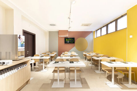 Bright dining area with white tables, wooden chairs, a coffee machine, and a TV screen at B&B Hotel Roma San Lorenzo Termini