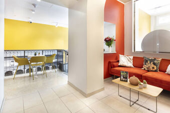Modern sitting area with orange sofa, cushions, table with plants, and yellow chairs near railing at B&B Hotel Roma San Lorenzo Termini