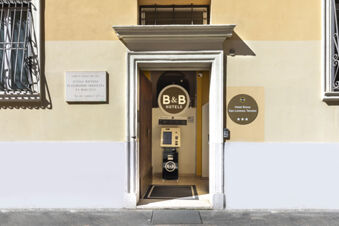Entrance of B&B Hotel Roma San Lorenzo Termini with open wooden door, signage, and a small kiosk inside the building