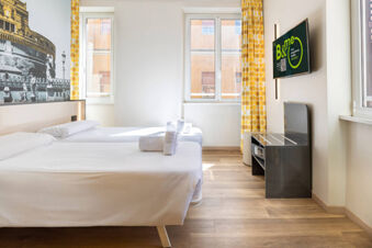 Two single beds with white linens and rolled towels in a bright room with yellow curtains and a TV at B&B Hotel Roma San Lorenzo Termini