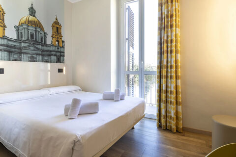 Bedroom with a double bed with white sheets and towels, a wall mural of a building, and yellow patterned curtains at B&B Hotel Roma San Lorenzo Termini