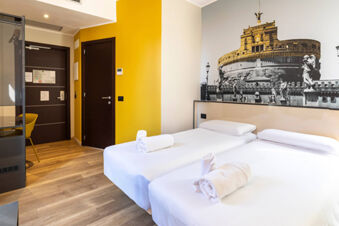 Twin beds with white linens and rolled towels in a bright room with yellow walls and B&B Hotel Roma San Lorenzo Termini mural