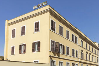 Three-story beige building with brown shutters and the B&B Hotel Roma San Lorenzo Termini sign on the roof against a clear blue sky