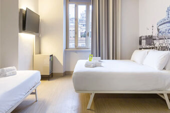 Two white beds with folded towels near a window and mounted TV in a room at B&B Hotel Roma Trastevere