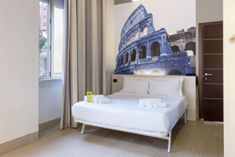 Room at B&B Hotel Roma Trastevere with a bed, white linens, folded towels, a large wall photo of the Colosseum, and a window