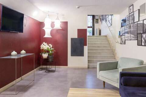 A lobby area at B&B Hotel Roma Trastevere with stairs, a TV, two table lamps, plants, two armchairs, and framed photos on the wall