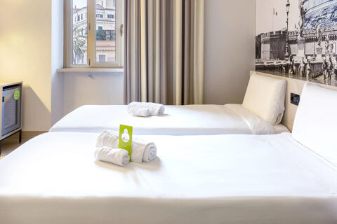 Hotel room at B&B Hotel Roma Trastevere with two single beds, white linens, rolled towels, a window, and a small fridge