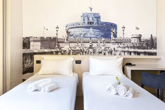 Two single beds with white linens and rolled towels in a room featuring wall art of Castel Sant'Angelo at B&B Hotel Roma Trastevere