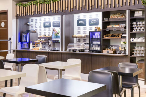 B&B Hotel Roma Trastevere breakfast buffet with coffee machine, baskets of croissants, yogurt fridge, and dining tables with chairs