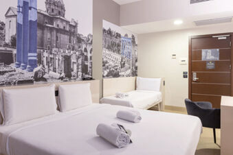 Hotel room at B&B Hotel Roma Trastevere with a double bed, single bed, black and white Rome-themed wall murals, and a wooden door