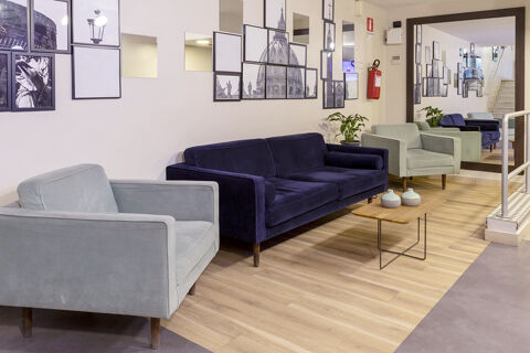 Seating area at B&B Hotel Roma Trastevere with a dark blue sofa, light grey armchair, wooden coffee table, and wall art panels