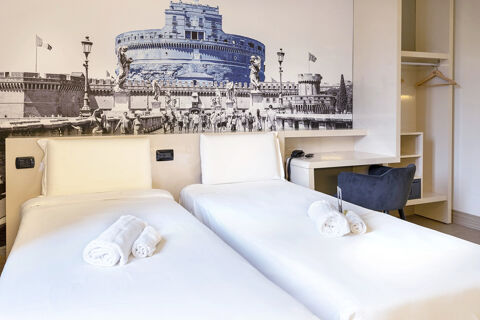 Two single beds with white linens and rolled towels in a room with a desk, chair, and B&B Hotel Roma Trastevere mural wall art