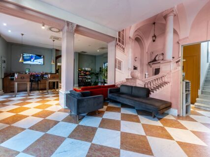 Spacious lobby area at B&B Hotel Genova Principe with check-in desks, dark and red sofas, columns, and a large mural wall image