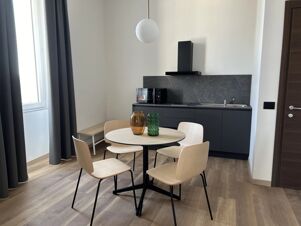 Modern kitchen and dining area with light wooden chairs, round table with vases, black cabinets, and microwave at B&B Hotel Genova Principe