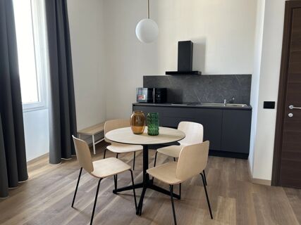 Modern kitchen and dining area with light wooden chairs, round table with vases, black cabinets, and microwave at B&B Hotel Genova Principe