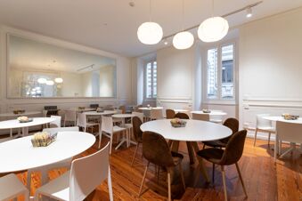 Dining area with white round tables, various chairs, pendant lights, large wall mirror, and wooden floor at B&B Hotel Genova Principe