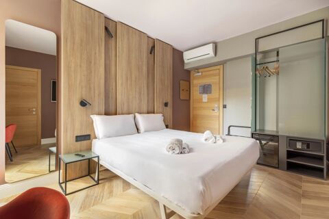 Double bed with two white pillows and rolled towels in a modern room at B&B Hotel Genova City Center with wooden furniture and hangers