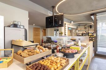 Breakfast buffet with croissants, muffins, donuts, and pastries displayed with coffee and condiments inside B&B Hotel Genova City Center
