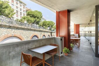 Outdoor seating area with modern tables and chairs along a corridor at B&B Hotel Genova City Center with stone wall view