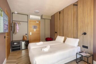 Twin beds with white linens and towels in a B&B Hotel Genova City Center room featuring wooden accents and a mounted TV