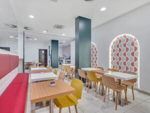Dining area at B&B Hotel Bergamo City with red bench seating, wooden tables, yellow and brown chairs, and patterned wall decor