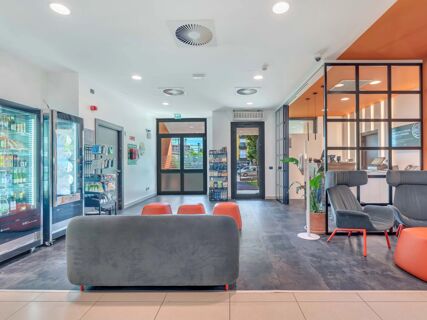Modern lobby area with grey and orange seating, vending machines, and glass reception desk at B&B Hotel Bergamo City
