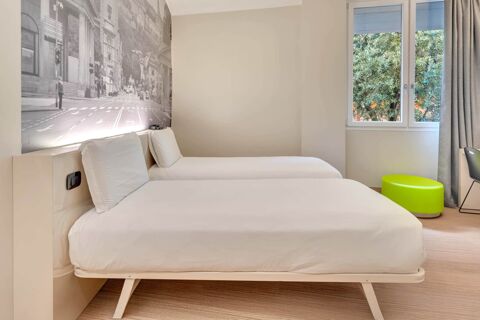 Two single beds with white linens and pillows are placed against a wall with a black and white cityscape mural at B&B Hotel Bergamo City