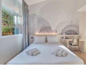 Double bed with white pillows and towels folded on it, window with gray curtains, desk with chair in B&B Hotel Bergamo City room
