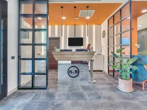 Reception area at B&B Hotel Bergamo City with a wooden desk, hanging lights, black-framed glass partitions, and a potted plant