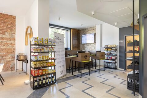 Modern reception area of B&B Hotel Brescia with snack shelves, two wooden reception desks, exposed brick wall, and large window light