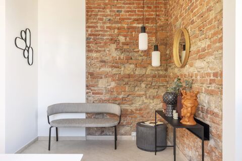 Interior corner of B&B Hotel Brescia with exposed brick walls, a gray bench, decorative vases, round mirror, and hanging lights