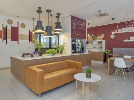 Lounge area with a tan leather sofa, small round tables with plants, hanging lights, and a coffee area in B&B Hotel Como Camerlata