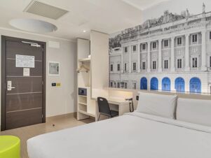 Hotel room at B&B Hotel Como Camerlata with a bed, desk, chair, closet with hangers, safe, and wall art of a classical building facade