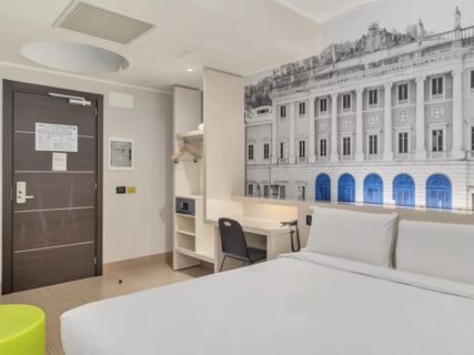 Hotel room at B&B Hotel Como Camerlata with a bed, desk, chair, closet with hangers, safe, and wall art of a classical building facade