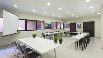 Meeting room with U-shaped white tables, black chairs, framed pictures, projector screen, and plants at B&B Hotel Como Camerlata
