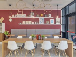 Dining area with wooden tables, white chairs, gray bench seating, red walls, decorative wall art, and lighting at B&B Hotel Como Camerlata