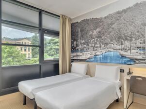 Two single beds with white linens in a bright room featuring a large window and a mural of boats over water at B&B Hotel Como Camerlata