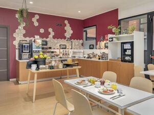 Breakfast buffet with cereals, fruits, coffee machine, and a dining area inside B&B Hotel Como Camerlata with maroon walls