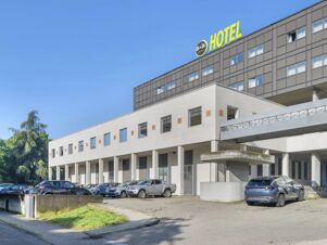 Modern building exterior with multiple windows, parked cars, and bright B&B Hotel Cremona signage on top under clear blue sky