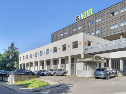 Modern building exterior with multiple windows, parked cars, and bright B&B Hotel Cremona signage on top under clear blue sky