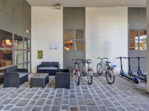 Outdoor seating area with black wicker sofa and armchairs next to parked bicycles and electric scooters at B&B Hotel Cremona