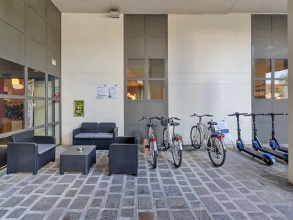 Outdoor seating area with black wicker sofa and armchairs next to parked bicycles and electric scooters at B&B Hotel Cremona