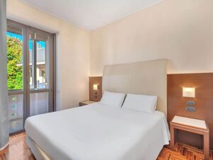Bedroom at B&B Hotel Habitat Giussano with a large bed, white linens, two pillows, wooden nightstands, and a glass door window