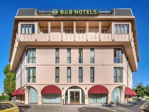 B&B Hotel Habitat Giussano building with beige facade, red awnings over ground floor windows, and clear blue sky background