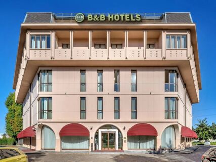 B&B Hotel Habitat Giussano building with beige facade, red awnings over ground floor windows, and clear blue sky background